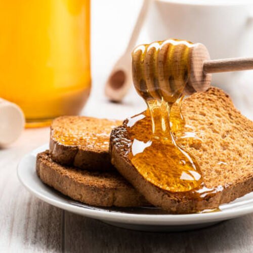 Honey dripping from wooden dipper on some wholemeal rusks.